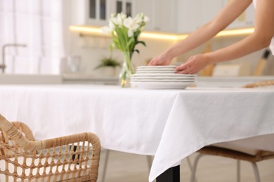 Photo of Woman putting plates on table with white tablecloth in kitchen, closeup