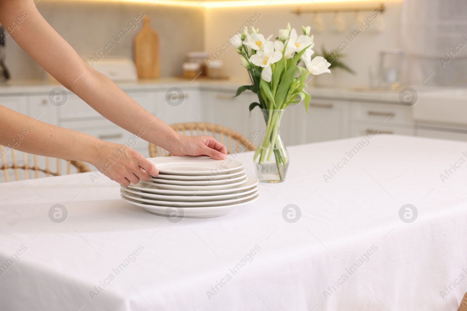 Photo of Woman putting plates on table with white tablecloth in kitchen, closeup