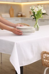 Photo of Woman putting plates on table with white tablecloth in kitchen, closeup