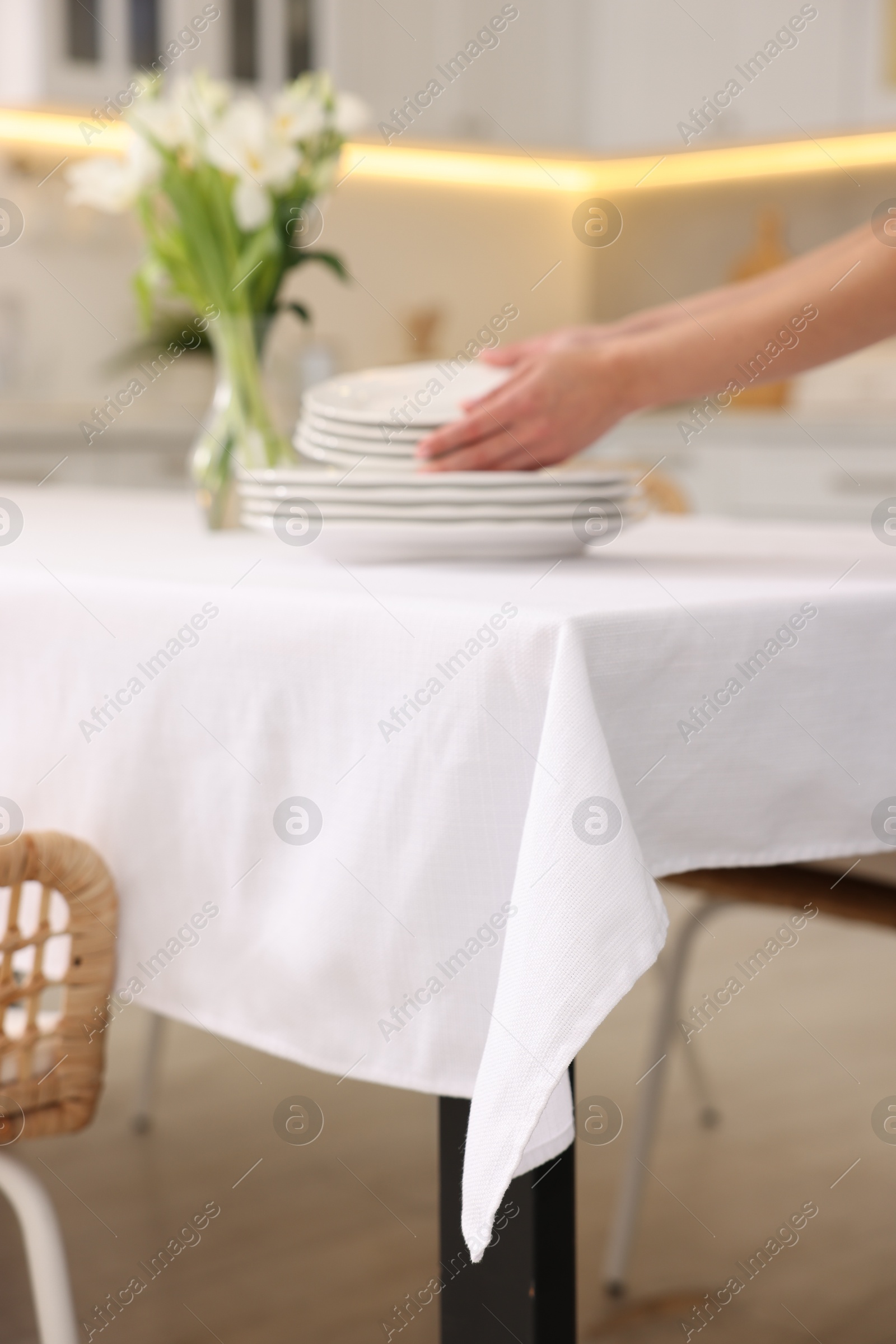 Photo of Woman putting plates on table with white tablecloth in kitchen, closeup