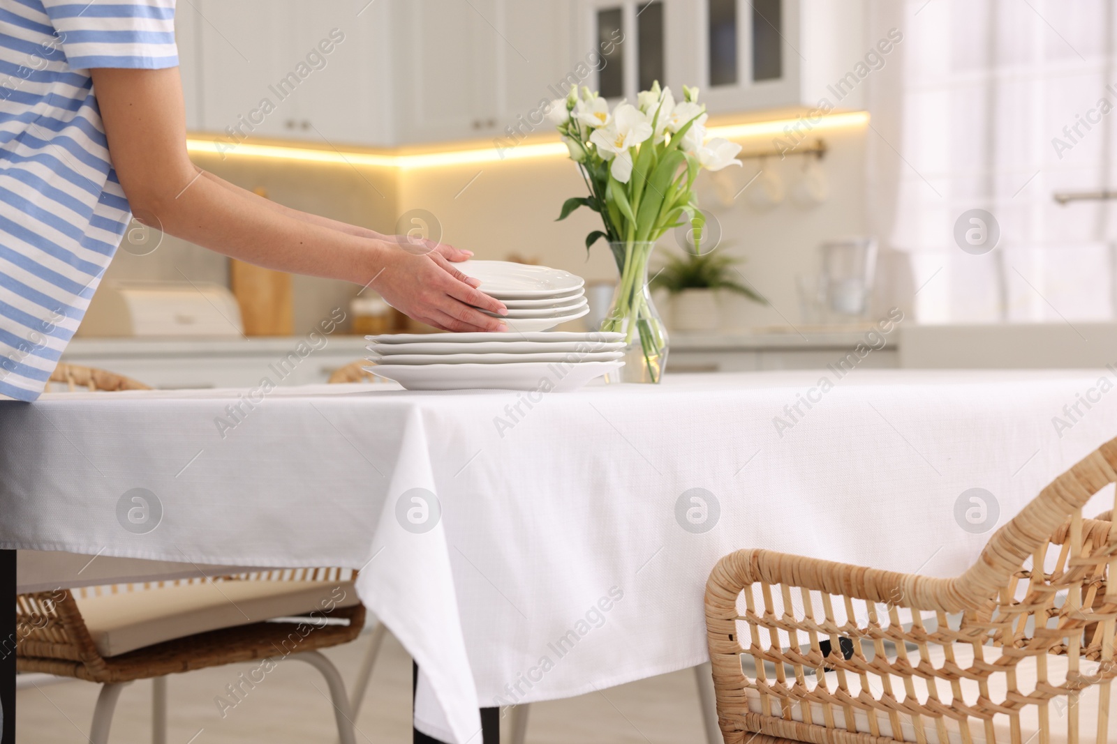 Photo of Woman putting plates on table with white tablecloth in kitchen, closeup