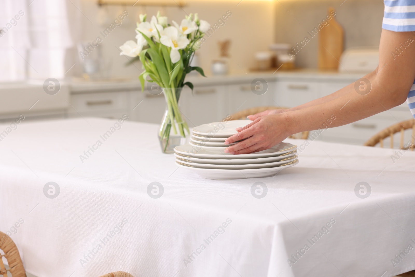 Photo of Woman putting plates on table with white tablecloth in kitchen, closeup