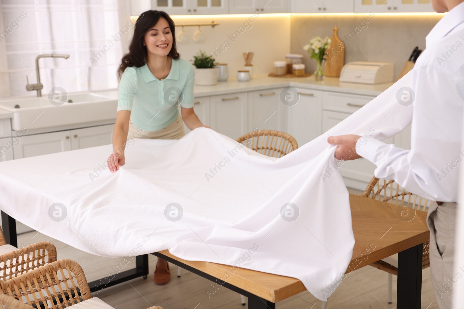 Photo of Couple putting white tablecloth on table in kitchen, selective focus