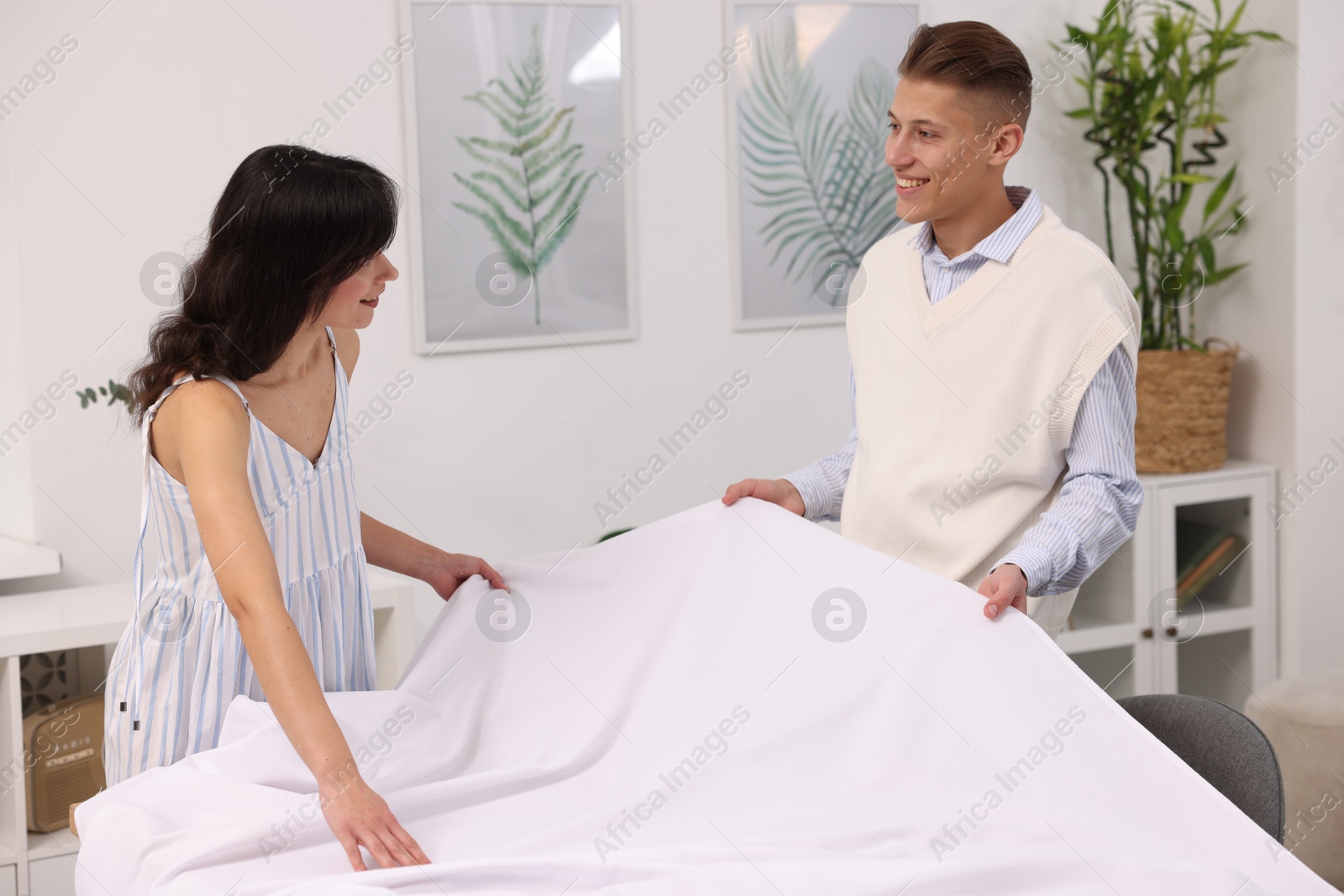 Photo of Couple putting white tablecloth on table at home