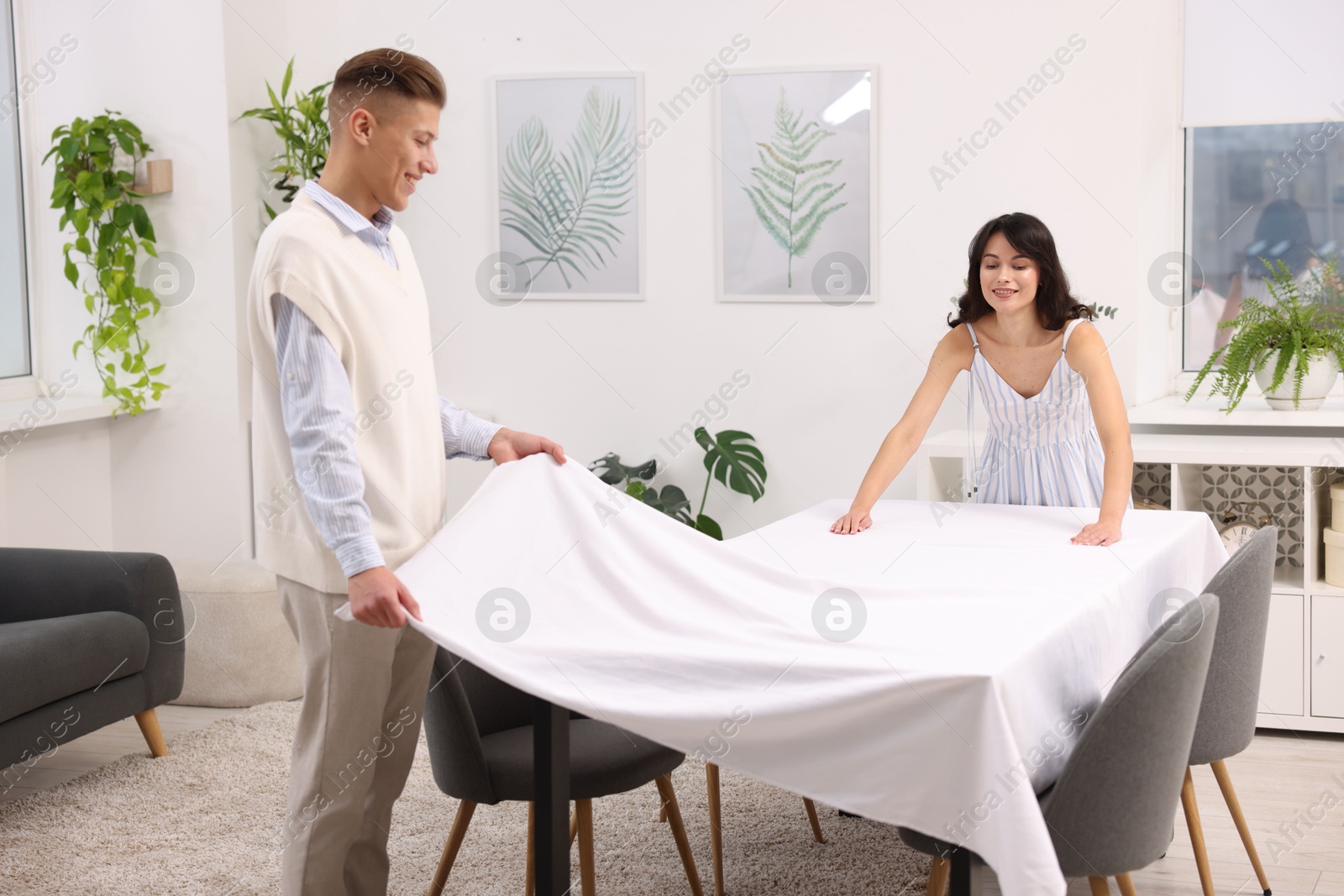 Photo of Couple putting white tablecloth on table at home