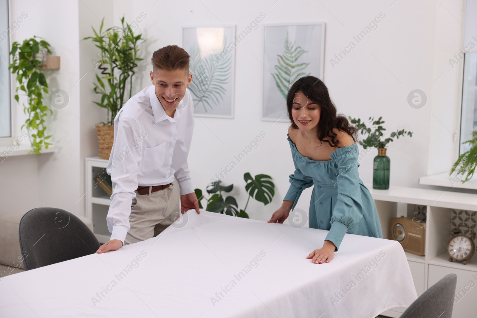 Photo of Couple putting white tablecloth on table at home