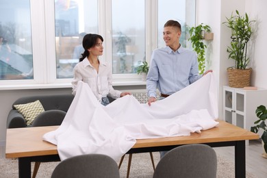 Photo of Couple putting white tablecloth on table at home