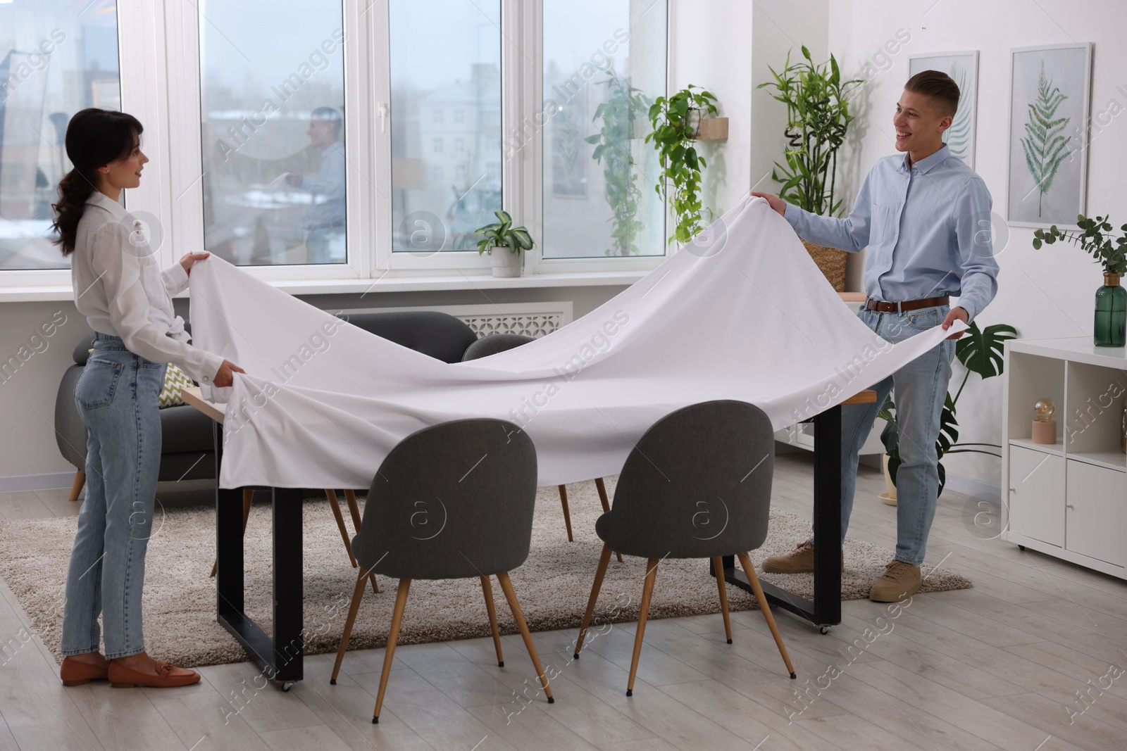 Photo of Couple putting white tablecloth on table at home