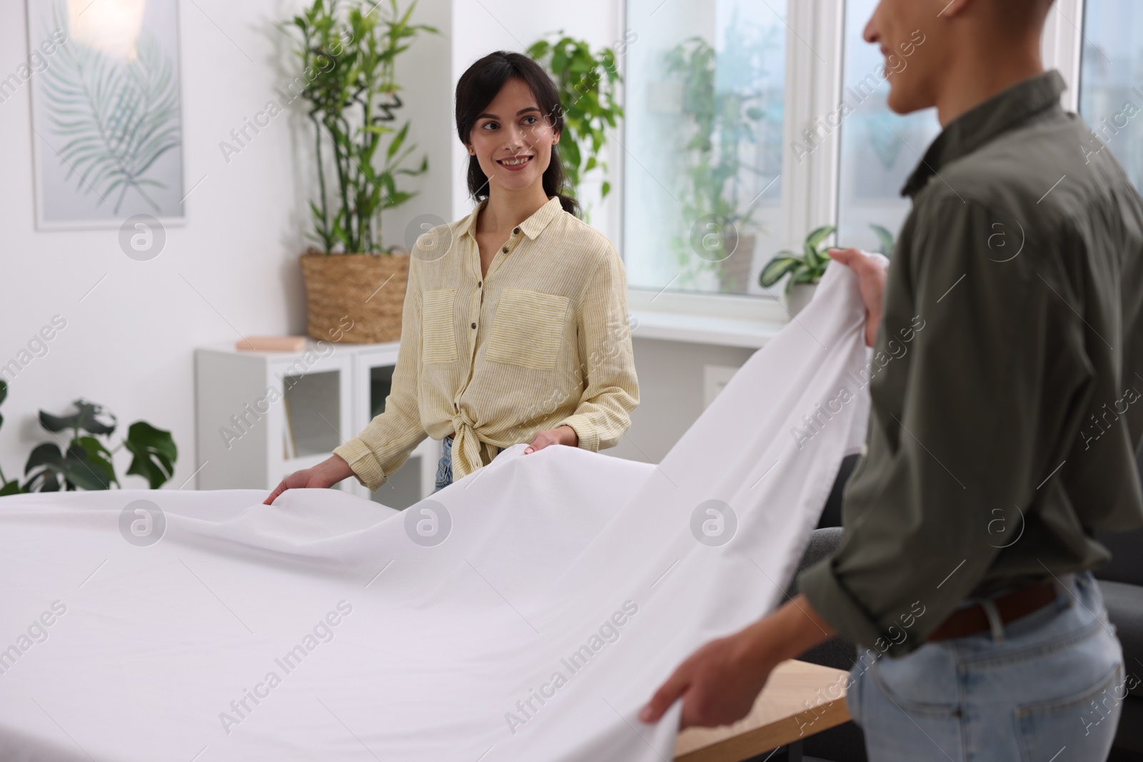 Photo of Couple putting white tablecloth on table at home