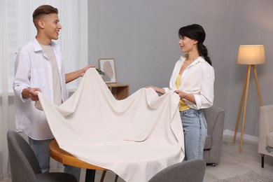 Photo of Couple putting white tablecloth on table at home