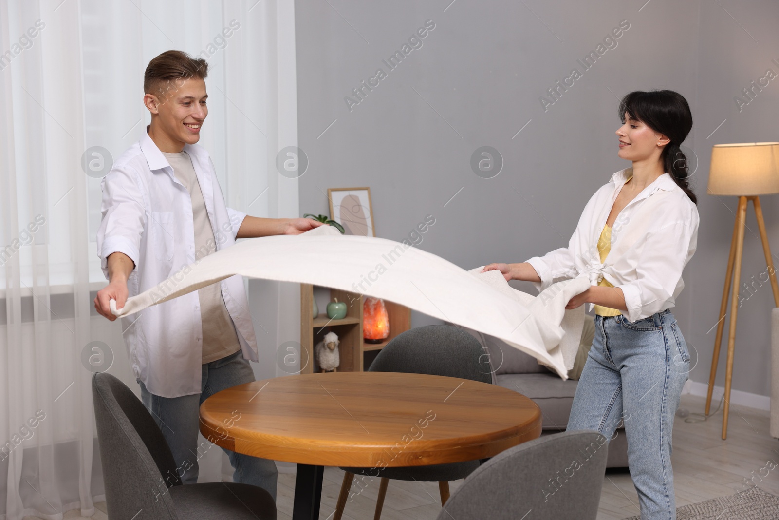 Photo of Couple putting white tablecloth on table at home