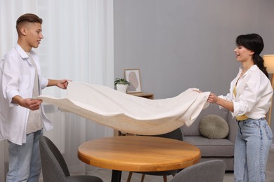 Photo of Couple putting white tablecloth on table at home