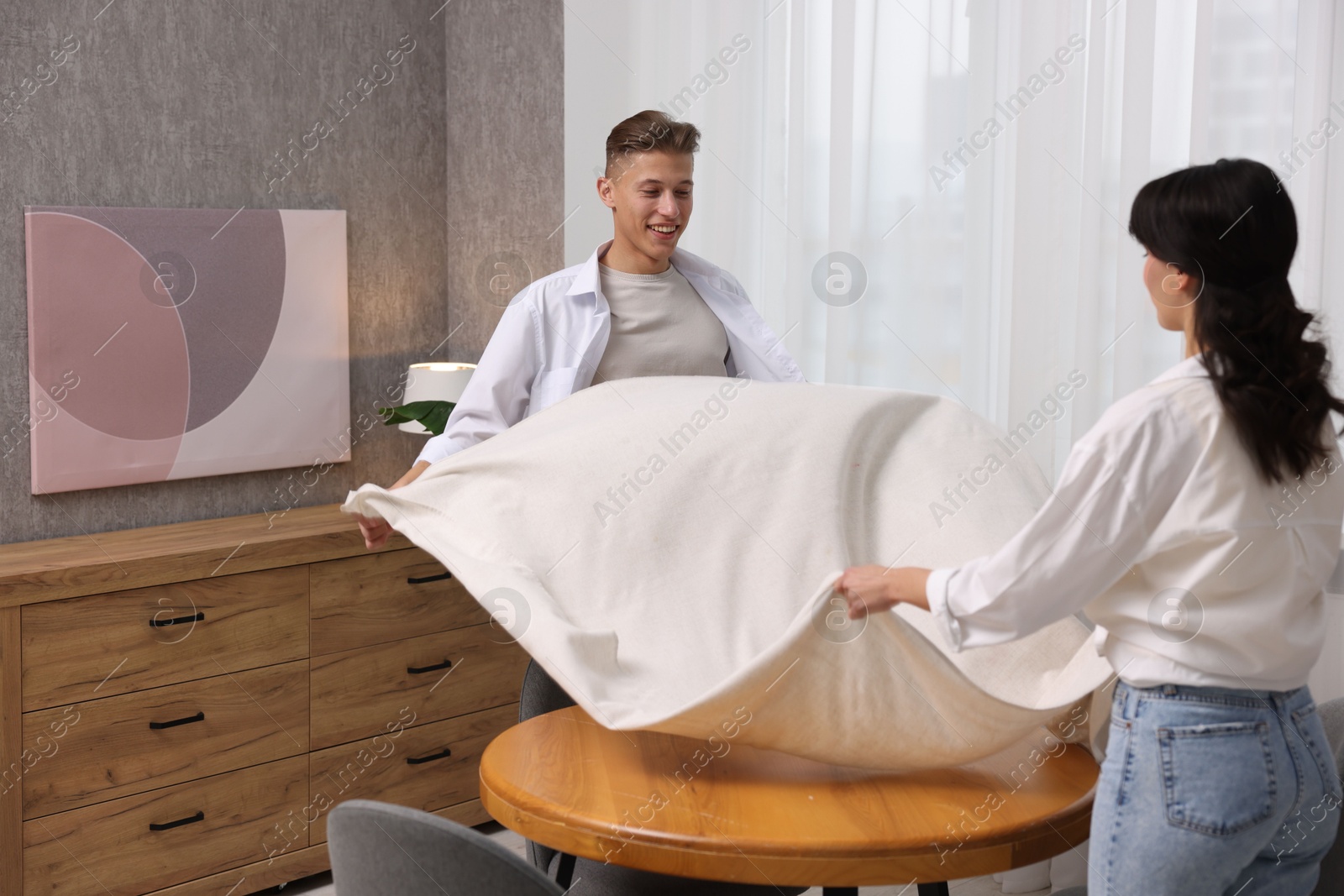 Photo of Couple putting white tablecloth on table at home