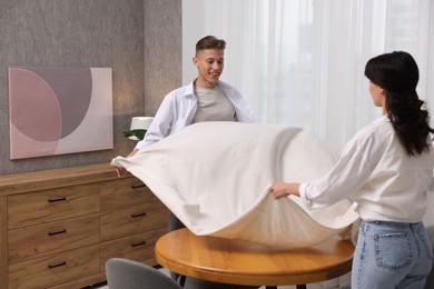 Photo of Couple putting white tablecloth on table at home