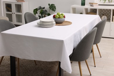 Photo of Table with white tablecloth, apples, plates and chairs in stylish room