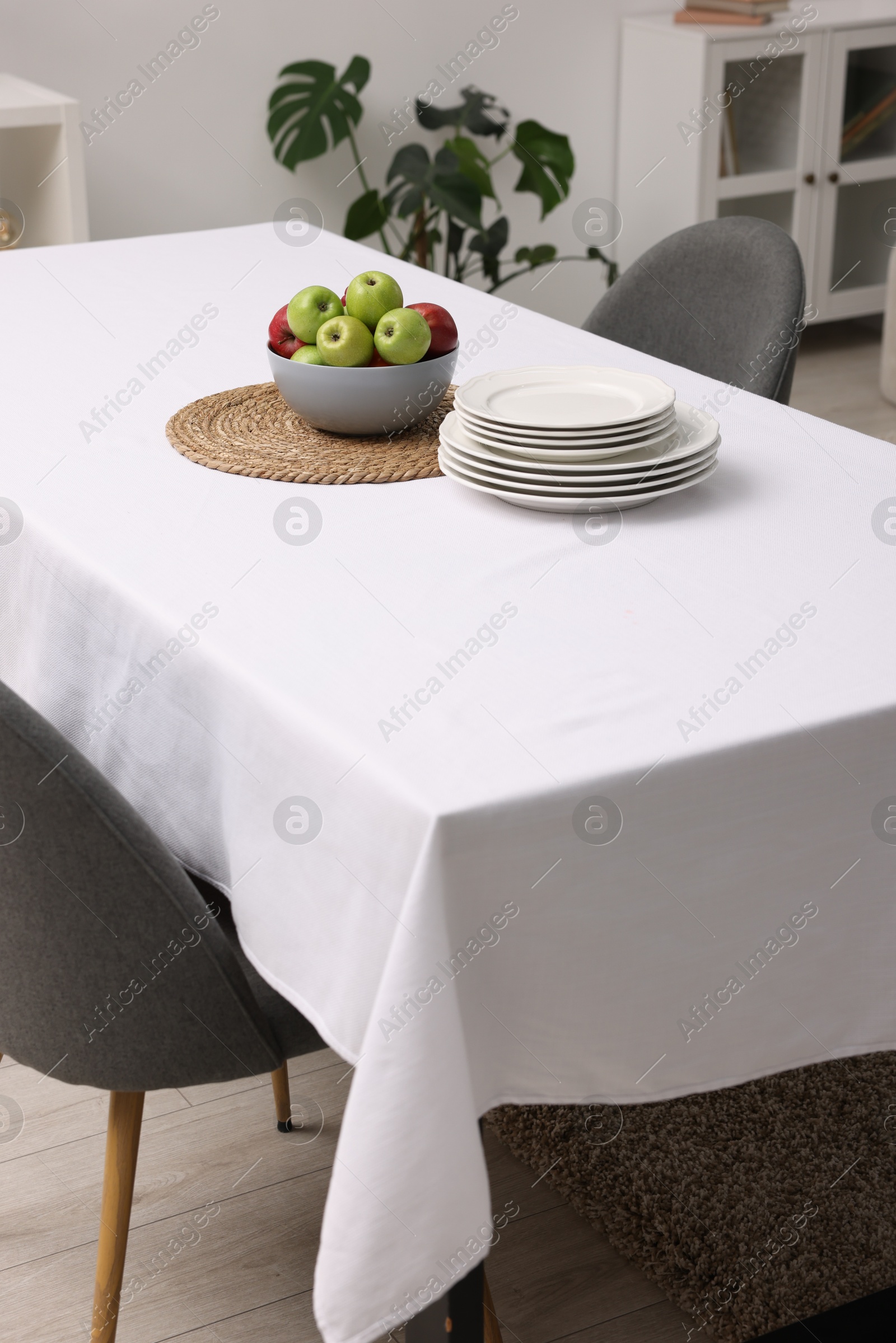 Photo of Table with white tablecloth, apples, plates and chairs in stylish room