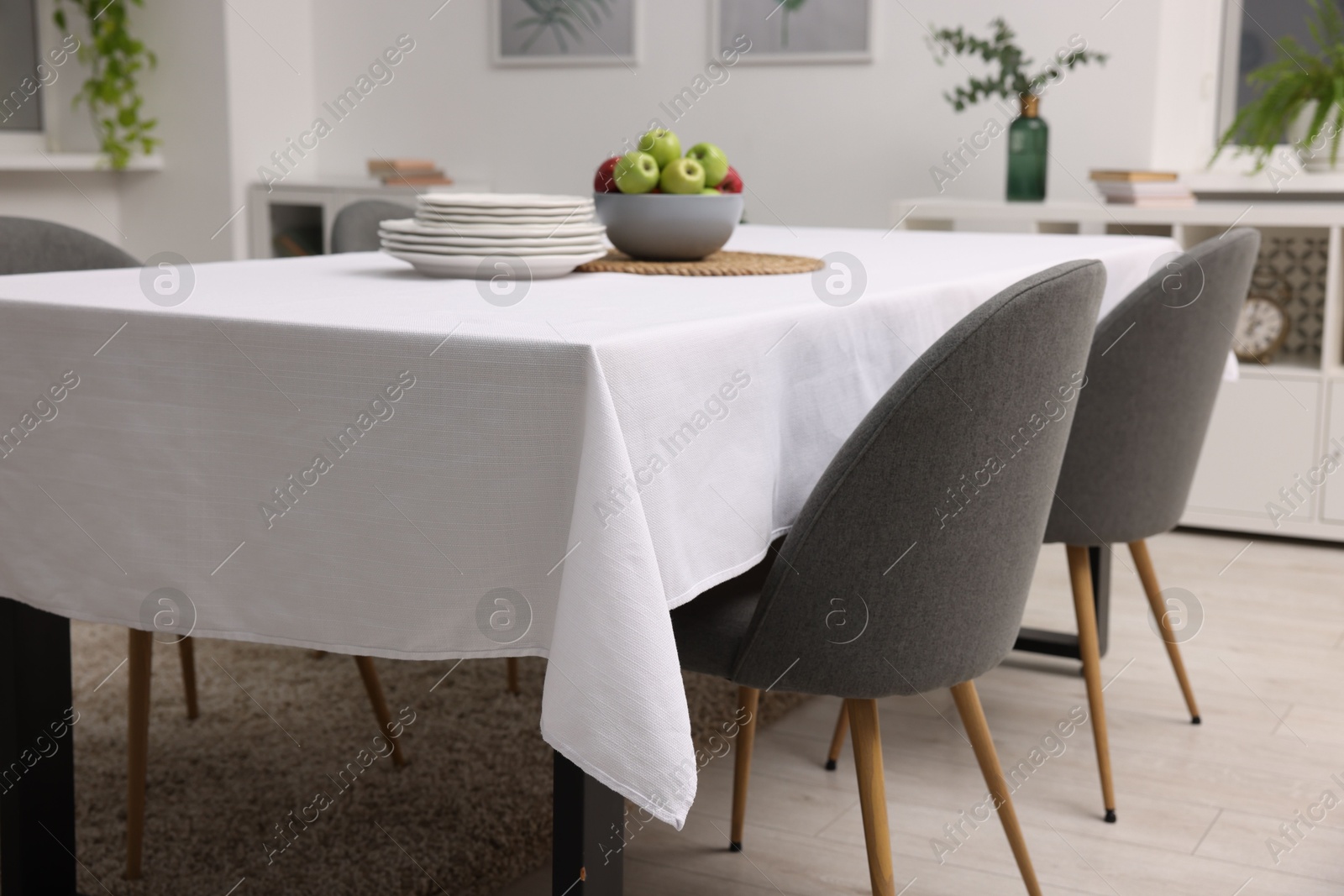 Photo of Table with white tablecloth, apples, plates and chairs in stylish room