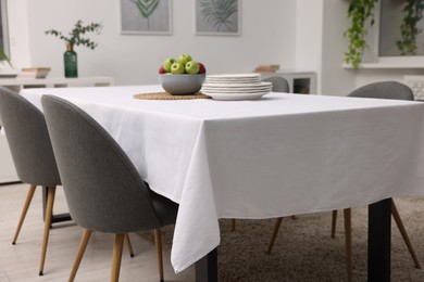 Photo of Table with white tablecloth, apples, plates and chairs in stylish room