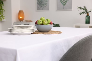 Photo of Table with white tablecloth, apples and plates in stylish room