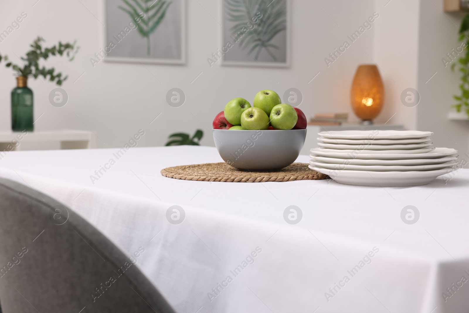 Photo of Table with white tablecloth, apples and plates in stylish room