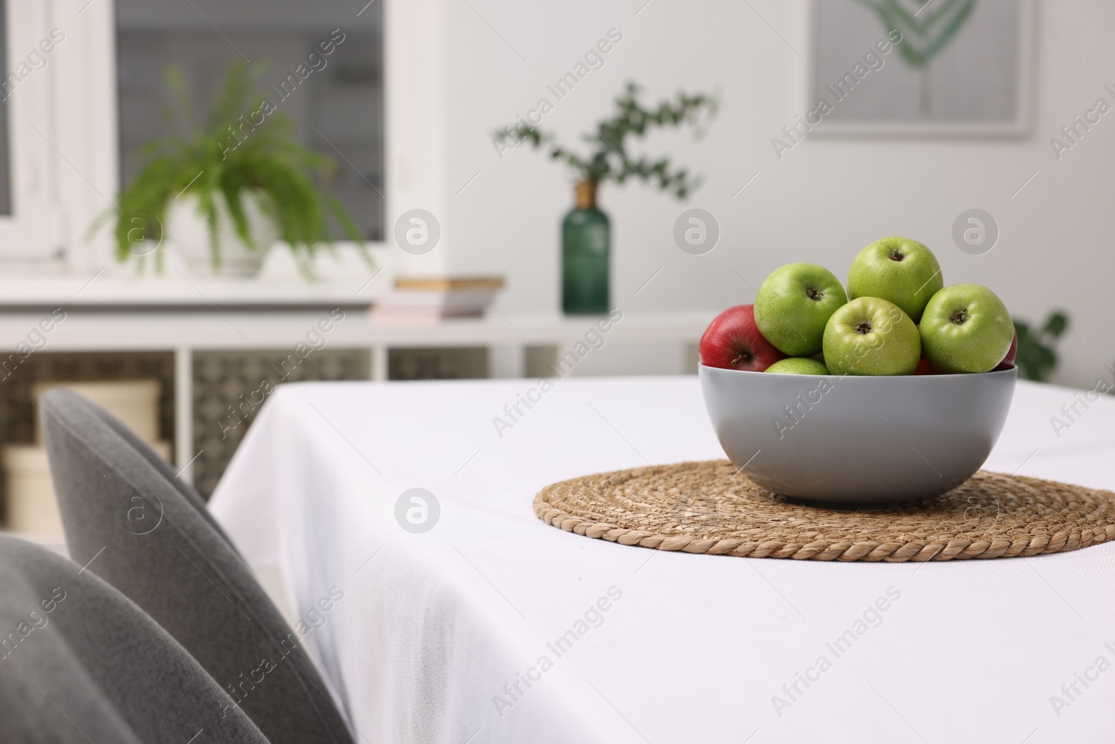 Photo of Bowl of apples on table with white tablecloth indoors