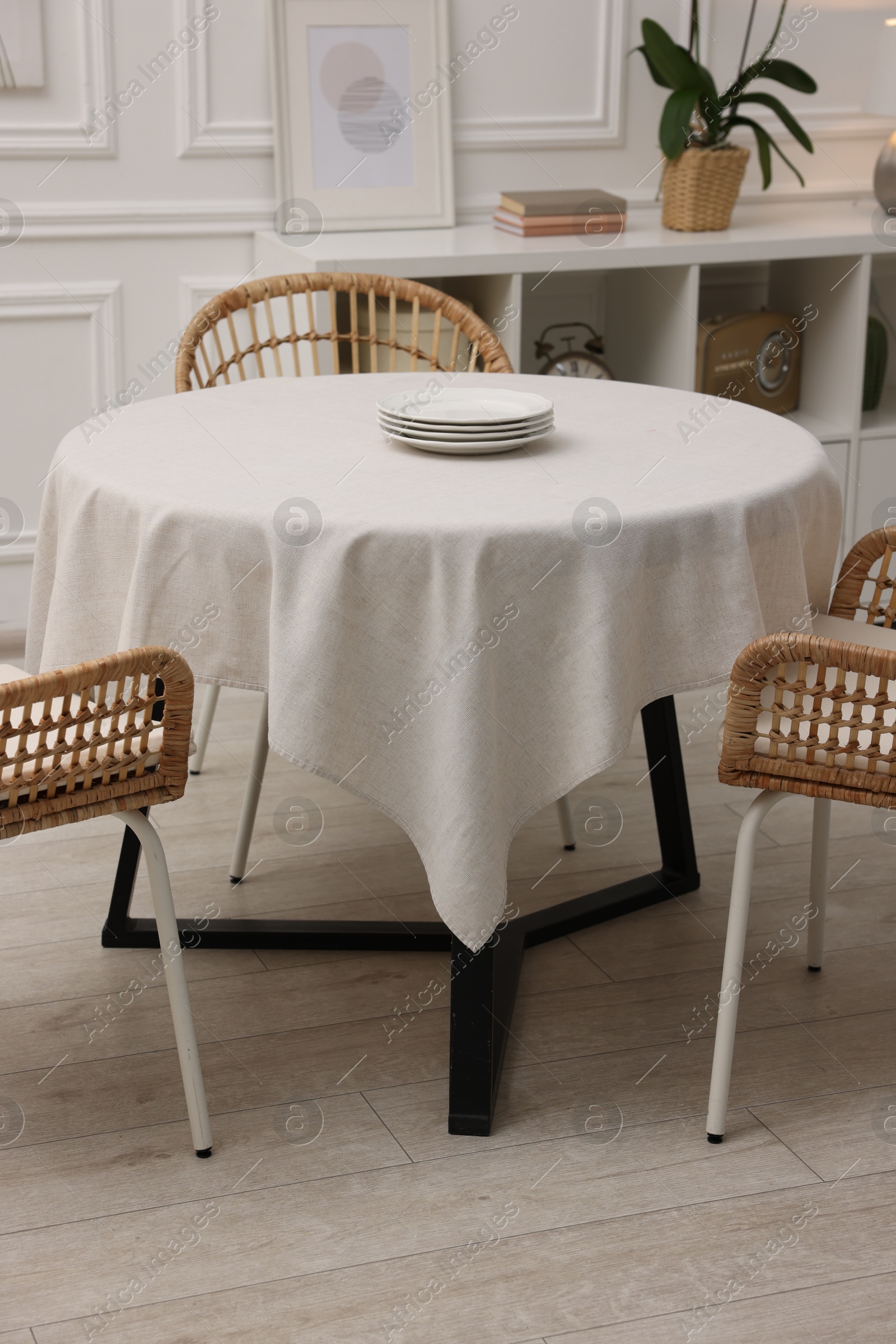 Photo of Table with white tablecloth, plates and chairs in stylish room. Interior design