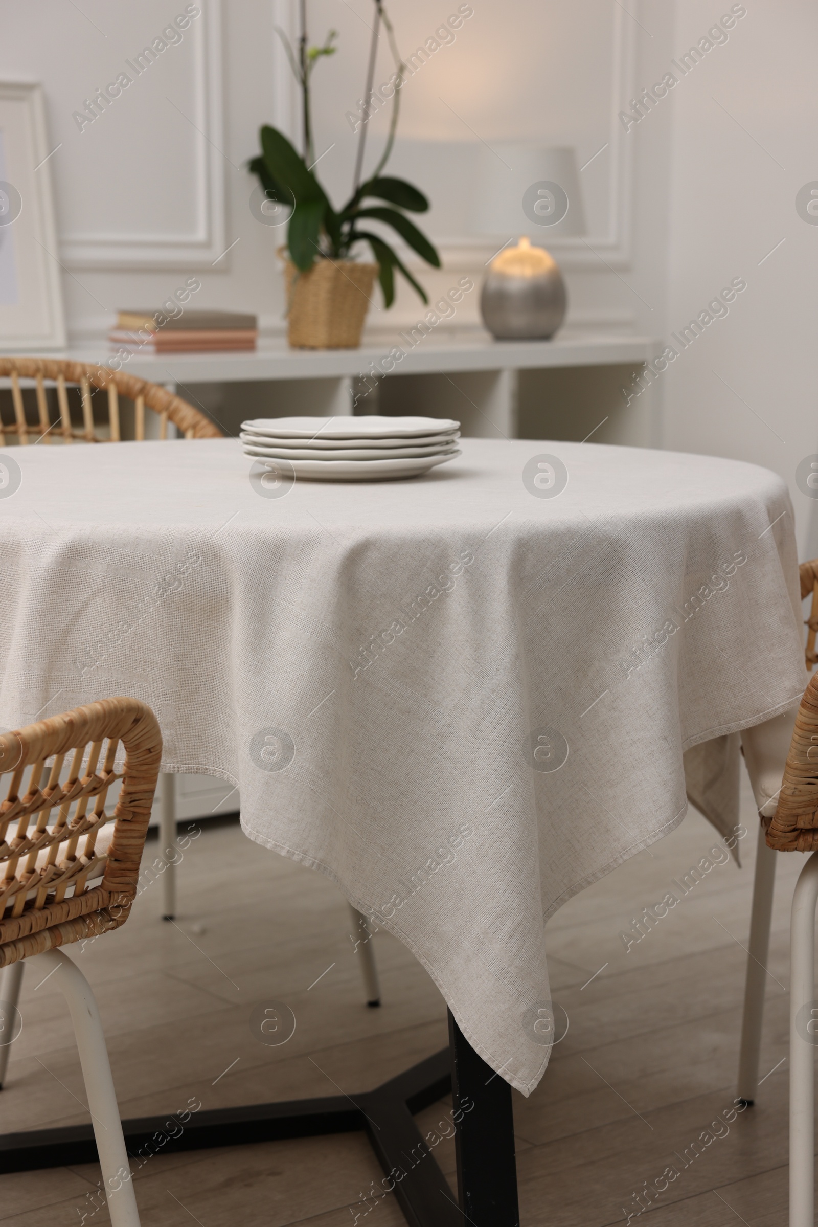 Photo of Table with white tablecloth, plates and chairs in stylish room. Interior design