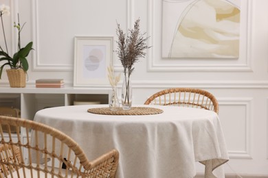 Photo of Table with white tablecloth, dried flowers in vases and chairs in stylish room. Interior design