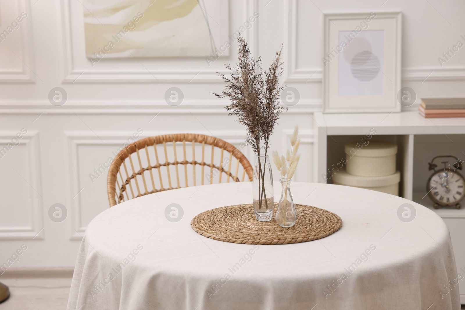 Photo of Table with white tablecloth and dried flowers in vases in stylish room. Interior design