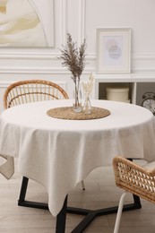 Photo of Table with white tablecloth, dried flowers in vases and chairs in stylish room. Interior design