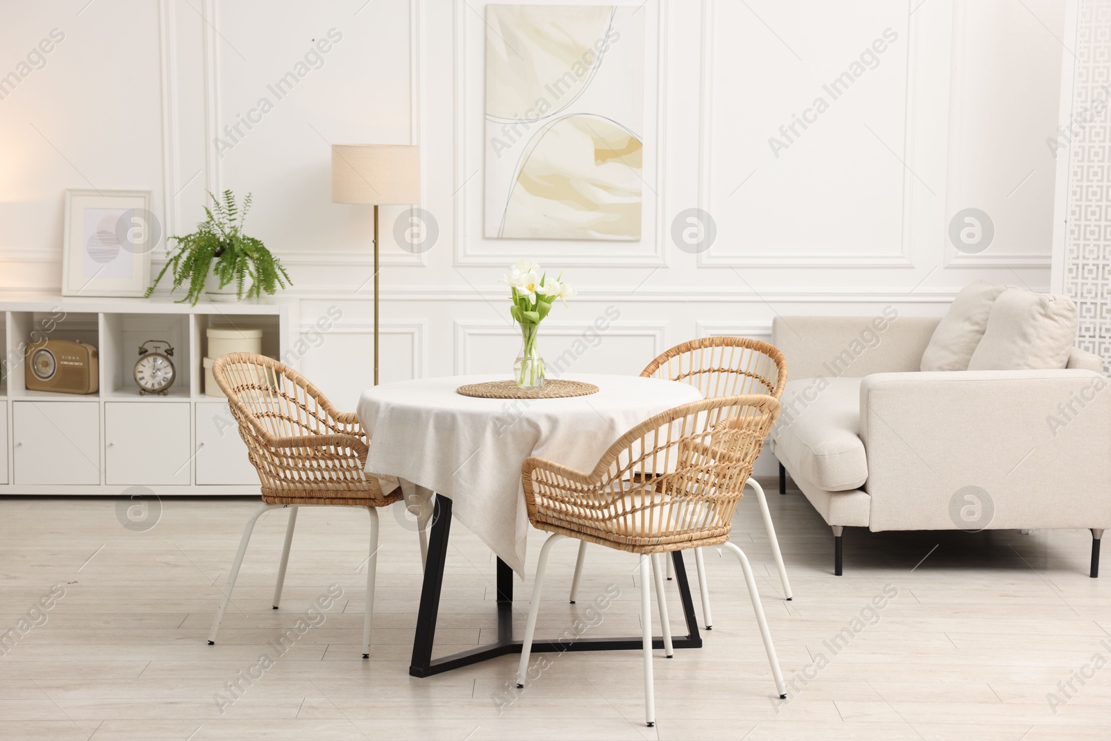 Photo of Table with white tablecloth, flowers in vase and chairs in stylish room. Interior design