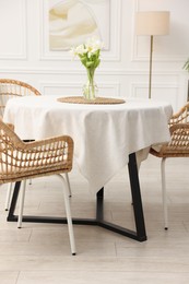 Photo of Table with white tablecloth, flowers in vase and chairs in stylish room. Interior design