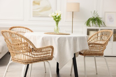 Photo of Table with white tablecloth, flowers in vase and chairs in stylish room. Interior design