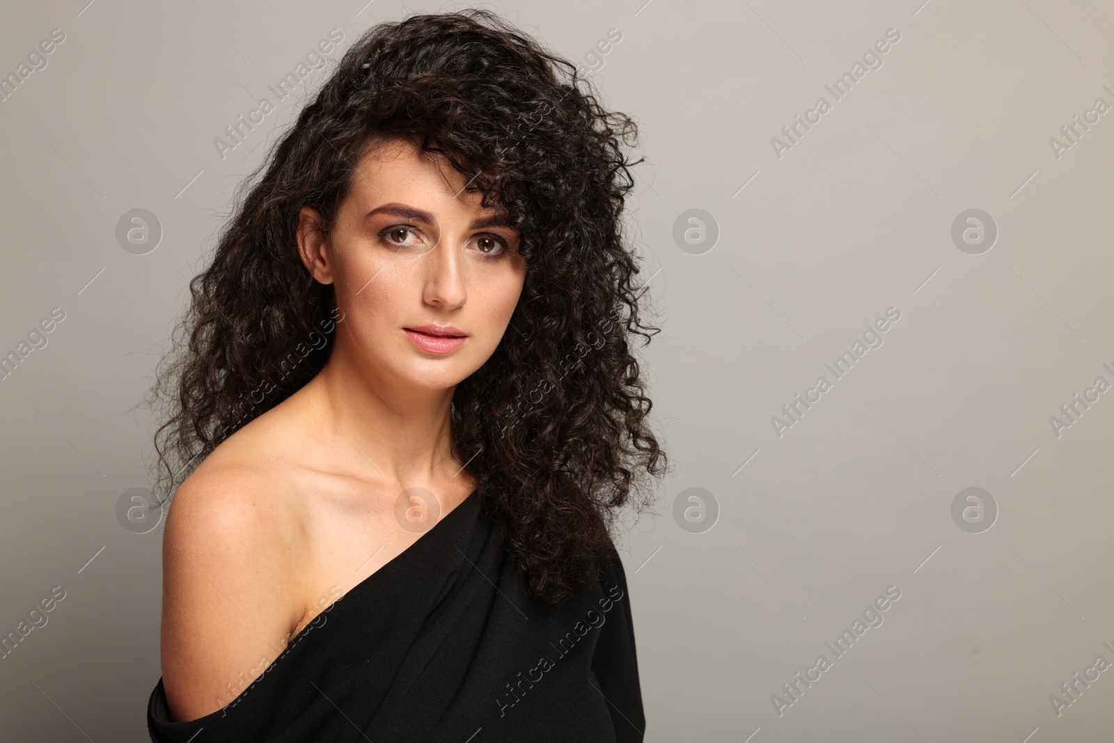 Photo of Beautiful young woman with long curly hair on light grey background. Space for text