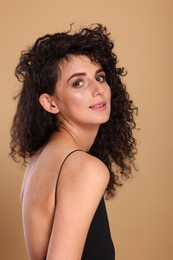 Photo of Beautiful young woman with long curly hair on beige background