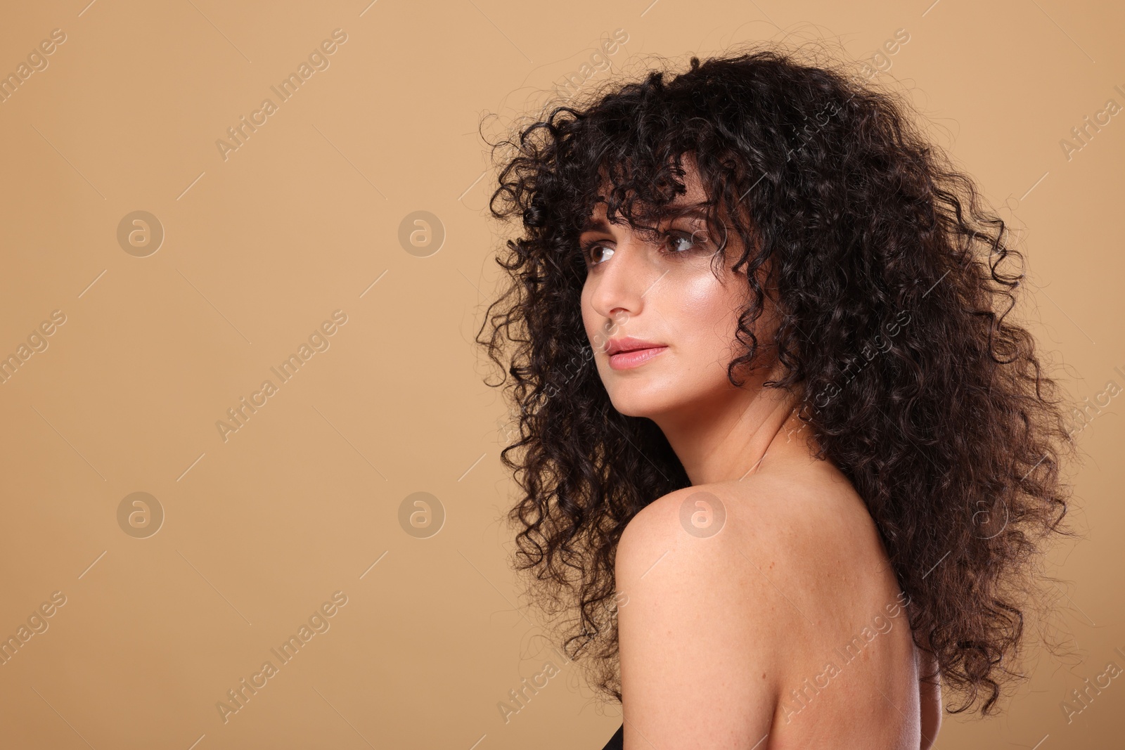 Photo of Beautiful young woman with long curly hair on beige background. Space for text