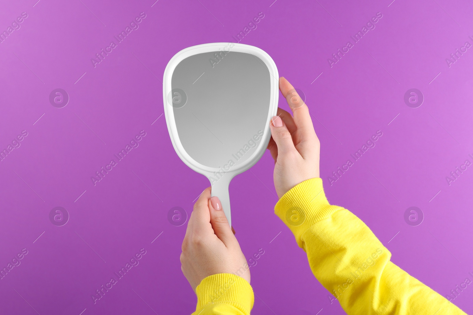 Photo of Woman holding handheld mirror on violet background, closeup