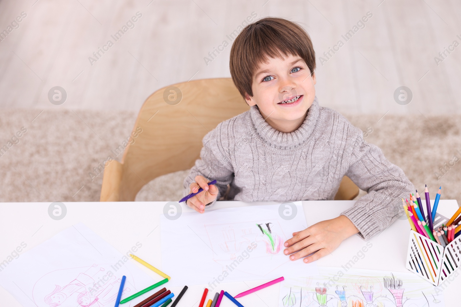 Photo of Happy boy drawing at white table indoors