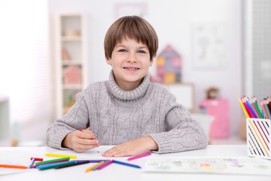 Photo of Happy boy drawing at white table in kindergarten