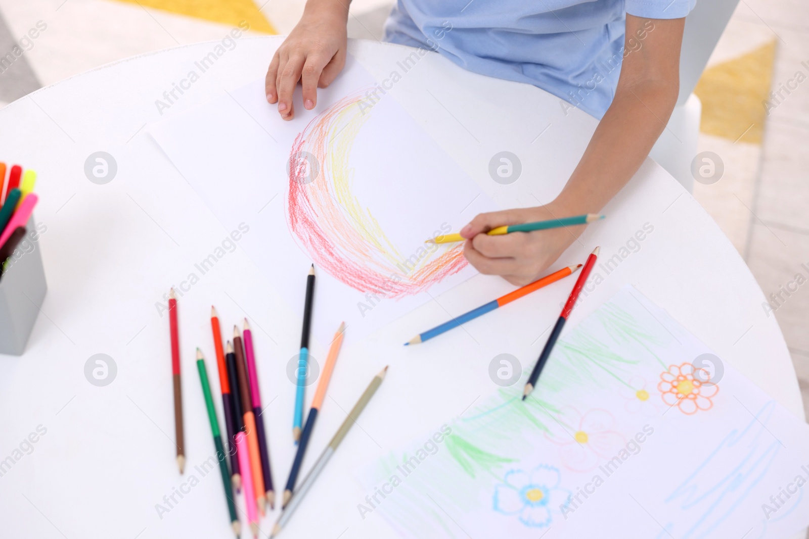 Photo of Boy drawing rainbow at white table, above view