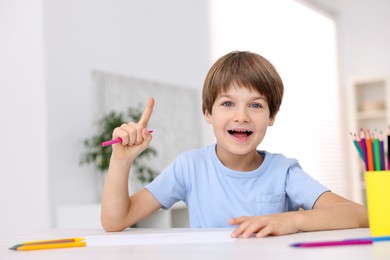 Photo of Happy boy had idea for his drawing at white table in kindergarten