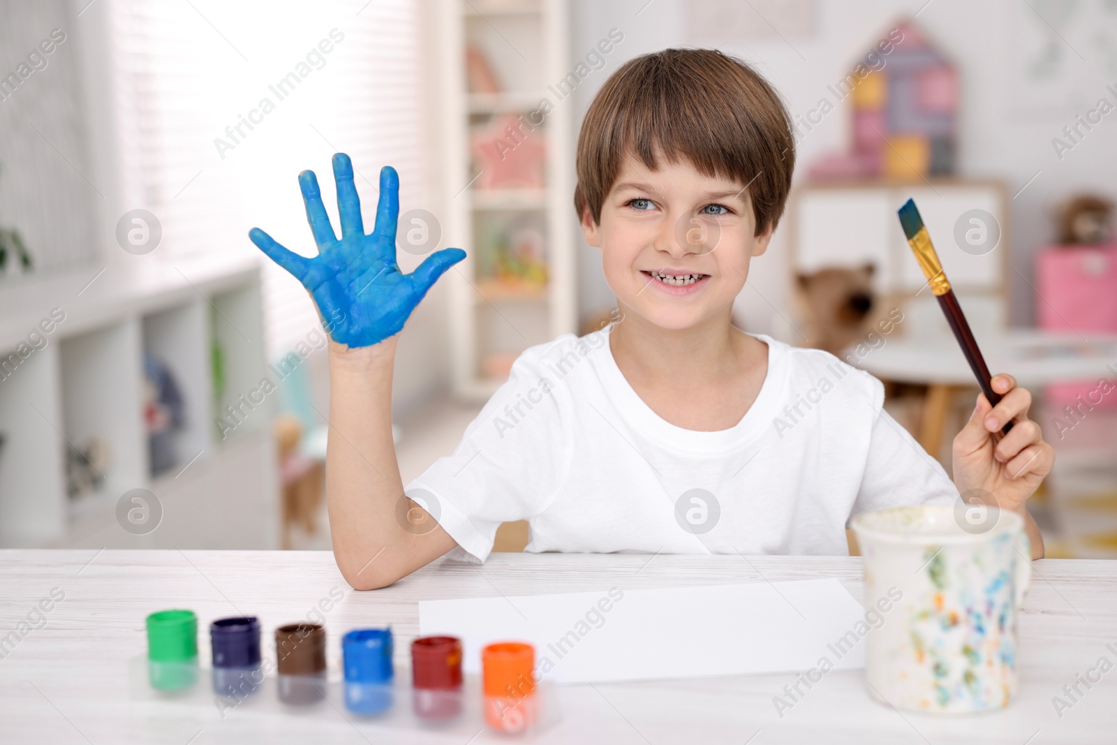 Photo of Happy boy drawing with palm at light wooden table in kindergarten