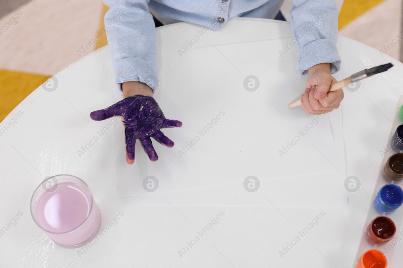 Photo of Girl drawing with palm at white table indoors, closeup