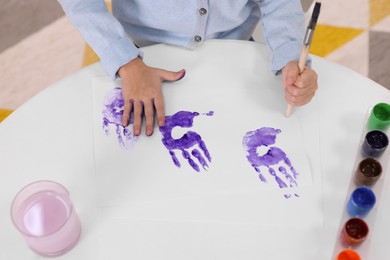 Photo of Girl drawing with palm at white table indoors, closeup