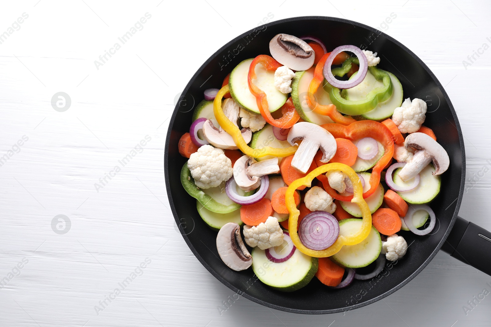 Photo of Frying pan with mix of vegetables and mushrooms on white wooden table, top view. Space for text