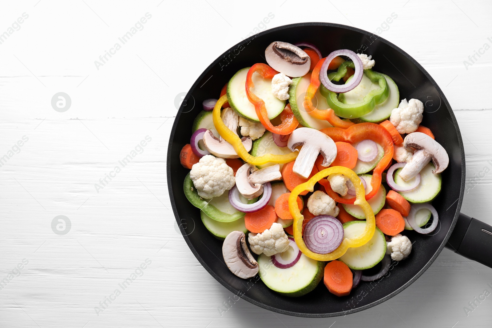 Photo of Frying pan with mix of vegetables and mushrooms on white wooden table, top view. Space for text