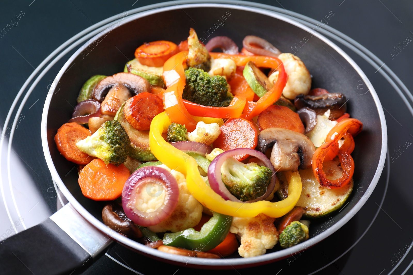 Photo of Frying pan with mix of vegetables and mushrooms on cooktop, closeup