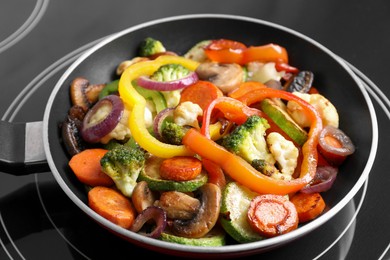 Photo of Frying pan with mix of vegetables and mushrooms on cooktop, closeup