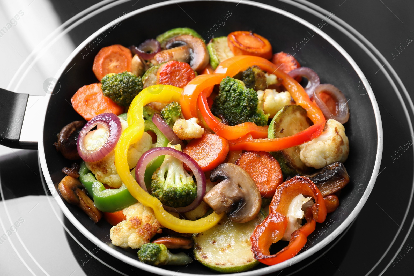 Photo of Frying pan with mix of vegetables and mushrooms on cooktop, closeup