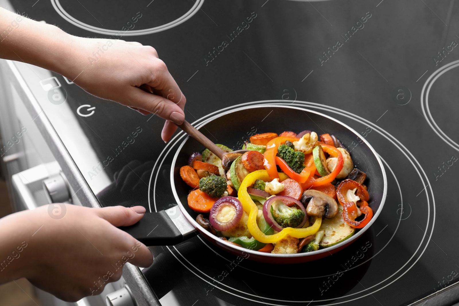 Photo of Woman cooking vegetables and mushrooms in frying pan on cooktop indoors, closeup